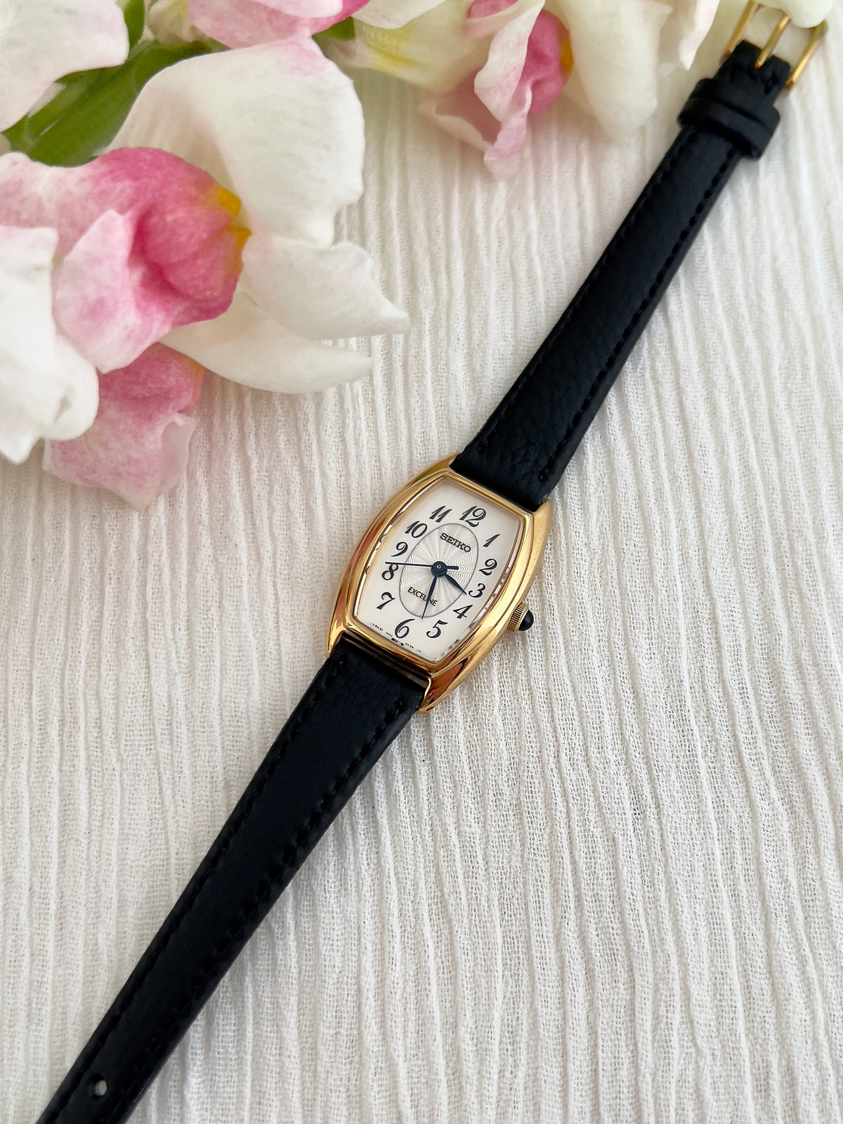 Seiko Exceline Gold Tonneau Women’s Watch with Arabic Dial — front view of tonneau case and black strap.