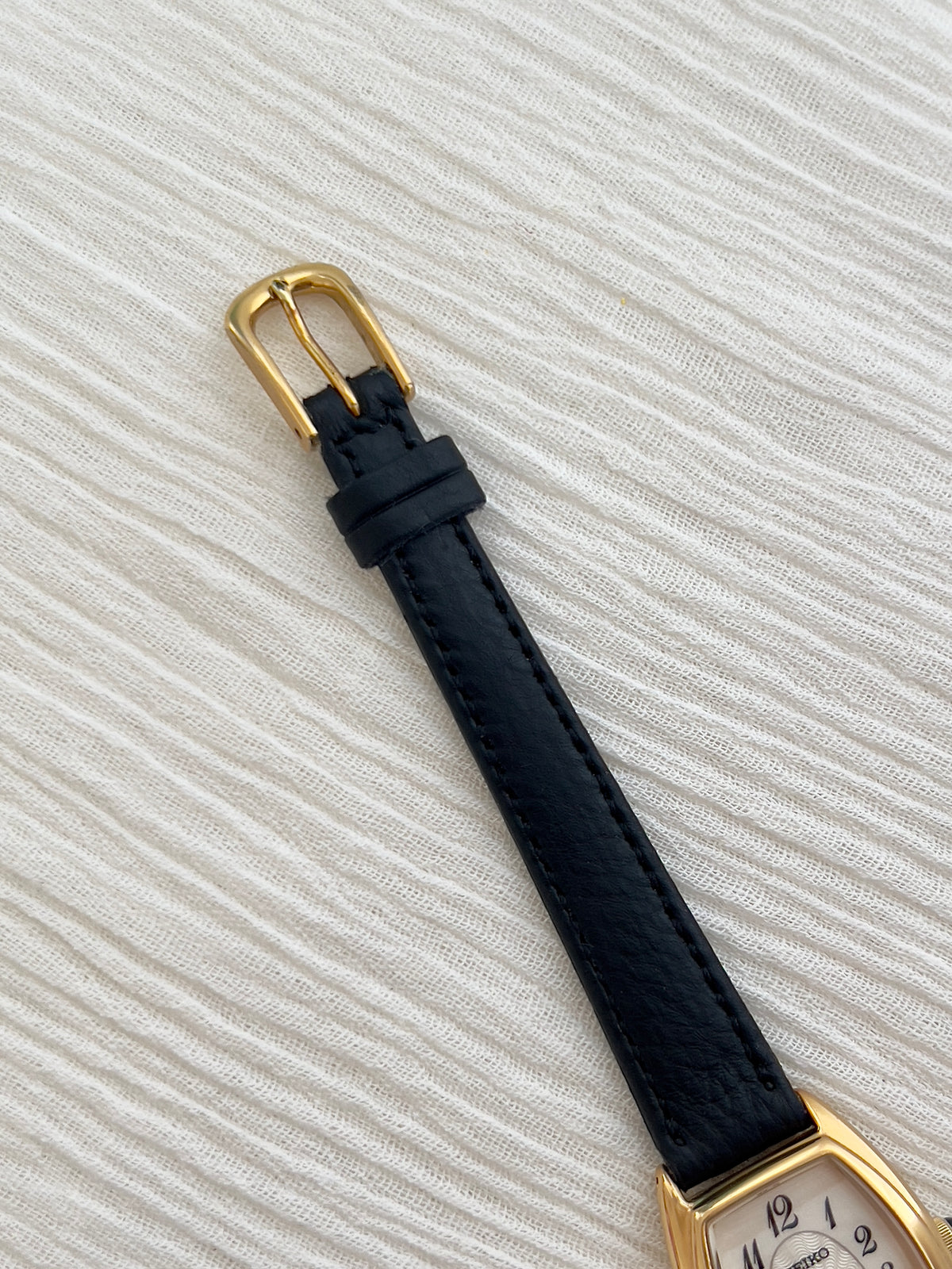 Seiko Exceline Gold Tonneau Women’s Watch with Arabic Dial — gold tone buckle and black strap.
