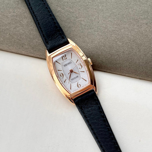 Seiko Exceline gold-tone tonneau watch with stardust-edge silver dial and black leather strap.