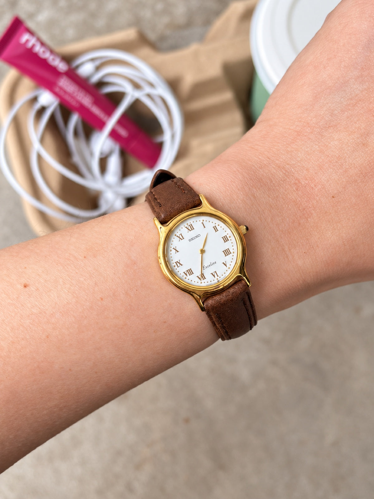 Seiko Exceline women's watch on wrist with a white Roman dial, gold tone round case and brown leather strap.