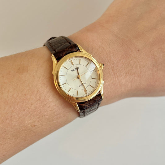 Seiko Exceline women’s watch worn on wrist featuring a gold tone case, white dial, brown leather strap and minimalist dress watch design