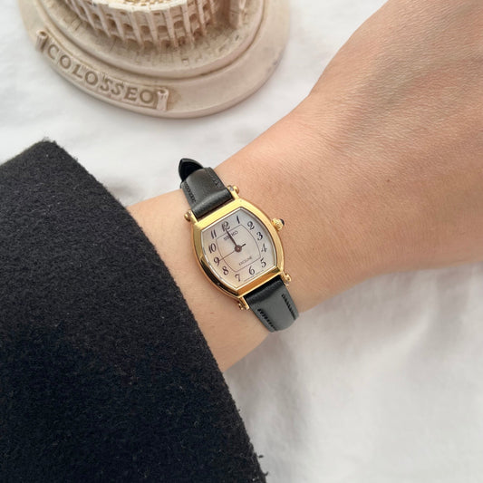 Vintage Seiko Exceline women’s watch worn on wrist featuring a mother of pearl dial, gold tone tonneau case, blue stone crown and black leather strap