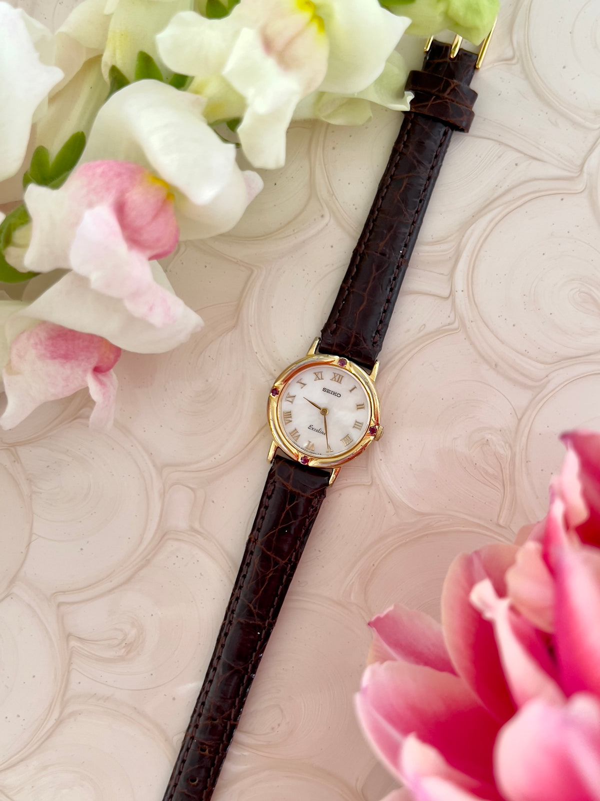 Seiko Exceline Mother of Pearl Women’s Watch with Ruby Accents — angled view of case and ruby accents.