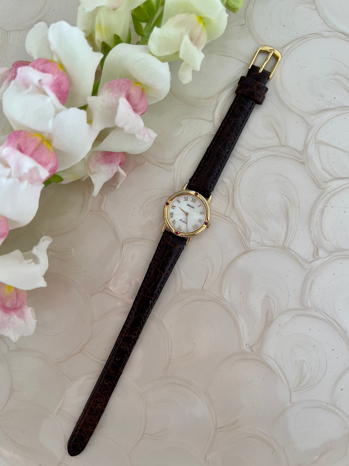 Seiko Exceline Mother of Pearl Women’s Watch with Ruby Accents — dial and textured leather strap.