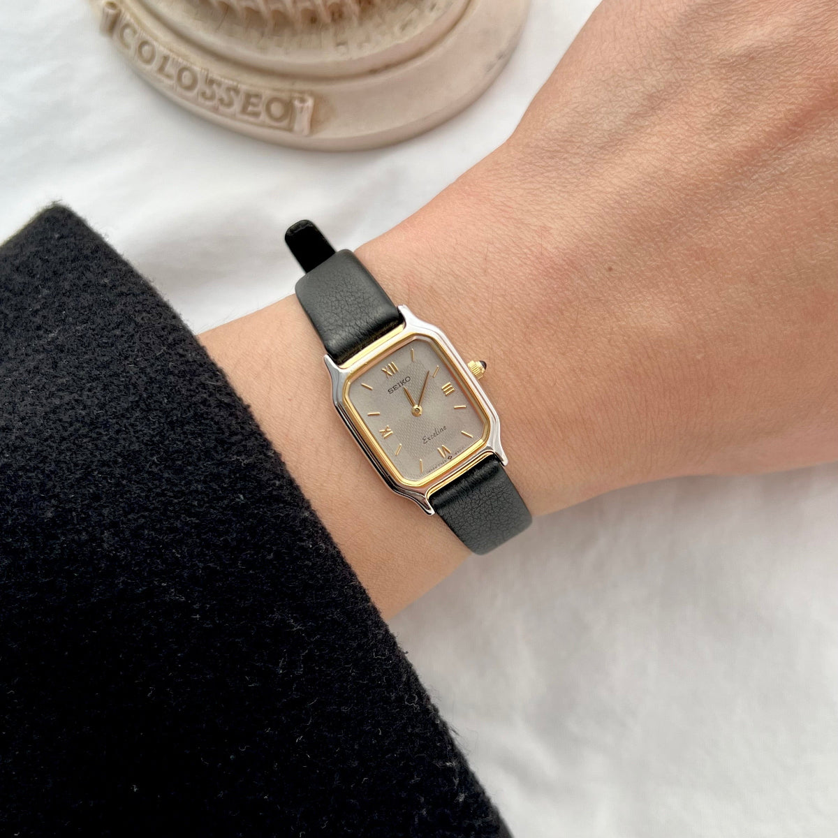 Seiko Exceline women’s watch worn on wrist featuring a two tone rectangular case, textured silver dial, Roman hour markers and black leather strap