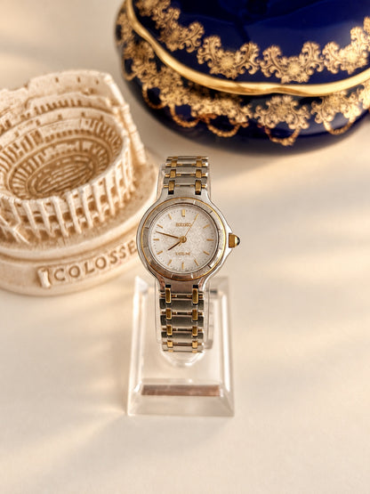Front view of the Seiko Exceline with a patterned white dial, gold tone baton markers and paired gold tone bracelet links.