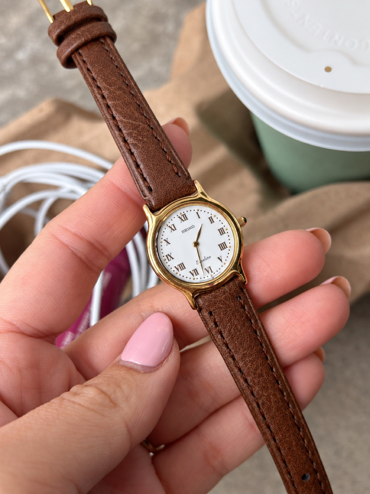 Seiko Exceline white Roman dial with raised gold tone dots, two pointed hands and curved gold tone lugs, held in a hand.