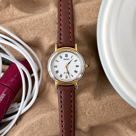Front of the Seiko Exceline white Roman dial watch with black leaf shaped hands, gold dot markers and two tone case.