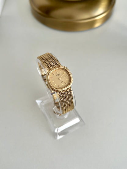 Full view of Seiko cushion watch on a clear stand showing the five row gold tone bracelet