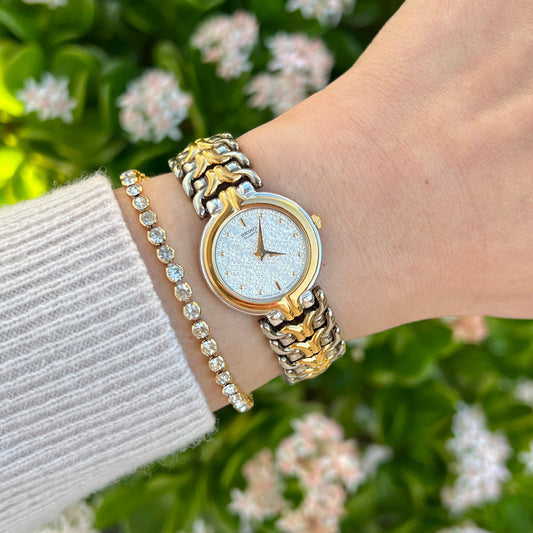 Seiko women’s watch with a silver floral dial and sculpted gold and silver tone bracelet worn on the wrist.