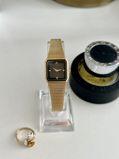 Seiko Galaxy women’s watch with a black panel dial, angular gold tone case and ribbed bracelet, shown front on.