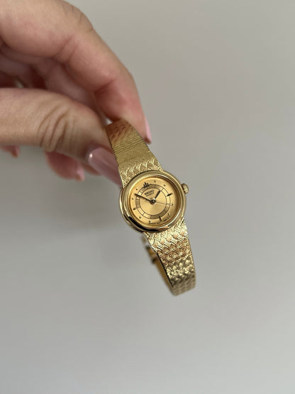 Angled view of the Seiko Galaxy polished gold tone bezel, fluted crown and basket weave bracelet.