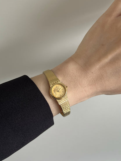 Seiko Galaxy champagne dial gold tone basket weave women’s watch worn on a wrist beside a black sleeve.