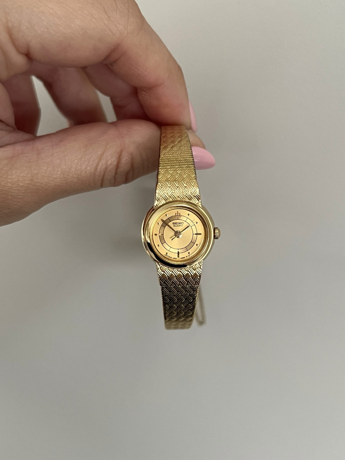 Upright front view of the Seiko Galaxy round gold tone case, Galaxy crest and textured integrated bracelet.