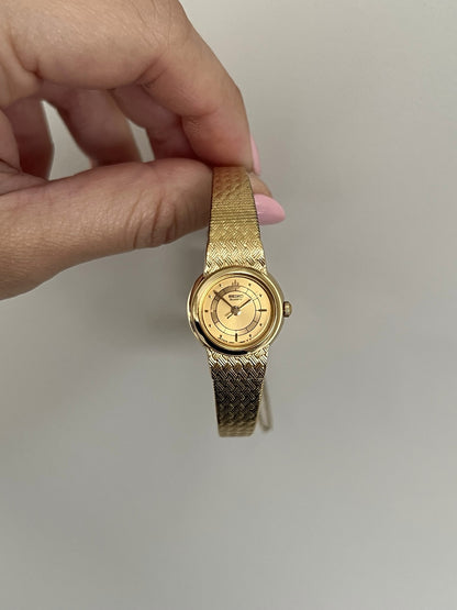 Upright front view of the Seiko Galaxy round gold tone case, Galaxy crest and textured integrated bracelet.