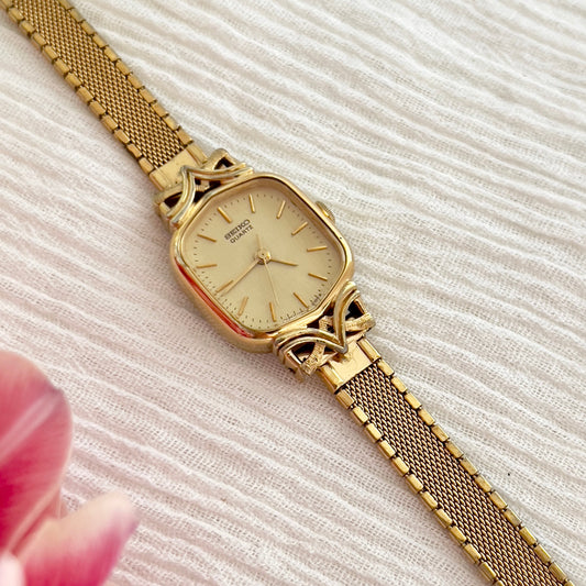 Seiko gold-tone watch with satin champagne dial displayed on a textured surface.