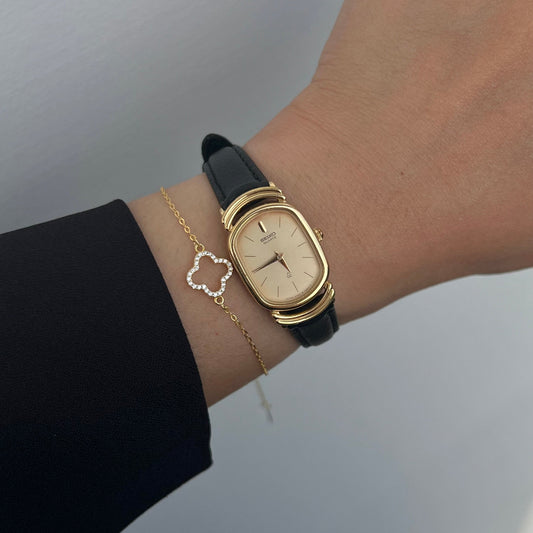 Seiko gold-tone oval watch with black leather strap shown on a wrist.