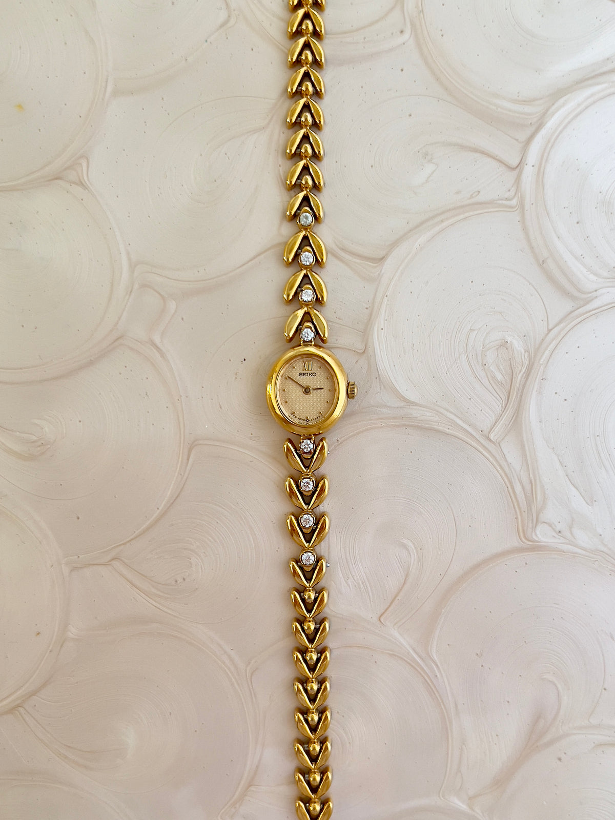 Seiko gold tennis bracelet watch shown on a wrist.