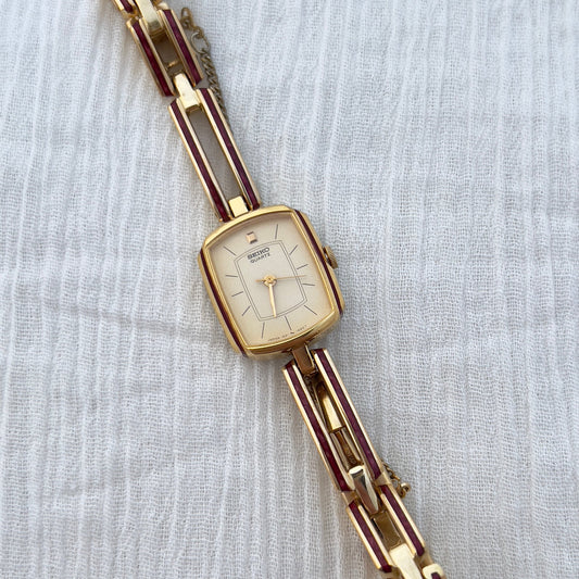 Seiko ladies gold bracelet watch with ruby enamel detailing and champagne dial worn on wrist beside diamond bracelet