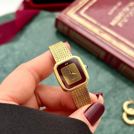 Seiko Lassale gold mesh watch with deep bordeaux dial held in a hand.