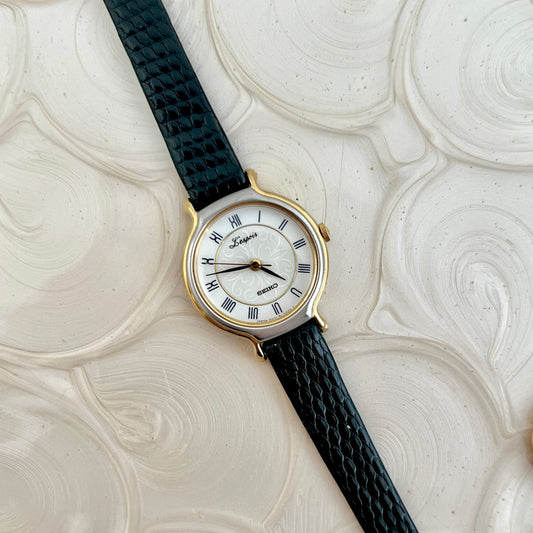 Seiko L'Espoir two-tone watch with black leather strap on a white graphic background.