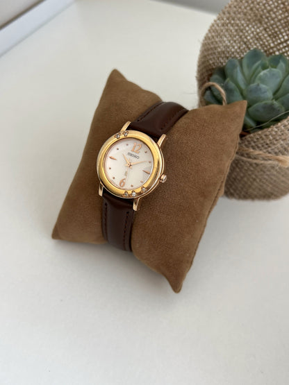 Angled front view Seiko Lukia women's watch with brushed champagne dial, five sparkling clear bezel stones and dark chocolate leather strap
