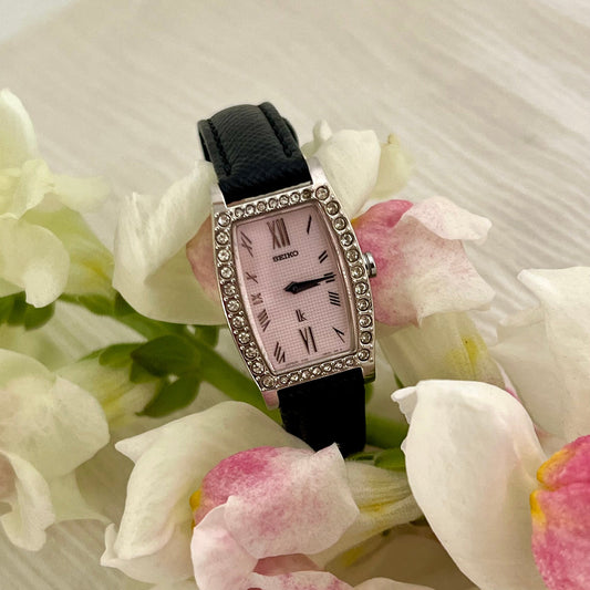 Seiko Lukia tonneau women's watch with pink dial, diamond-set bezel and black leather strap.