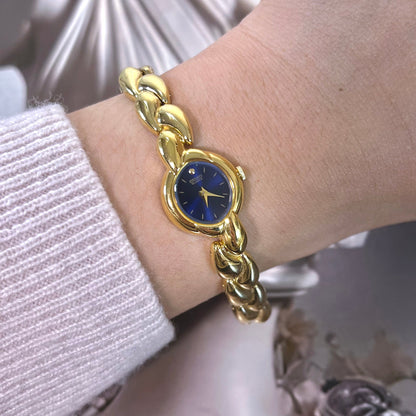 Seiko women’s watch with midnight blue sunburst dial, gold tone round case and sculptural petal link bracelet.