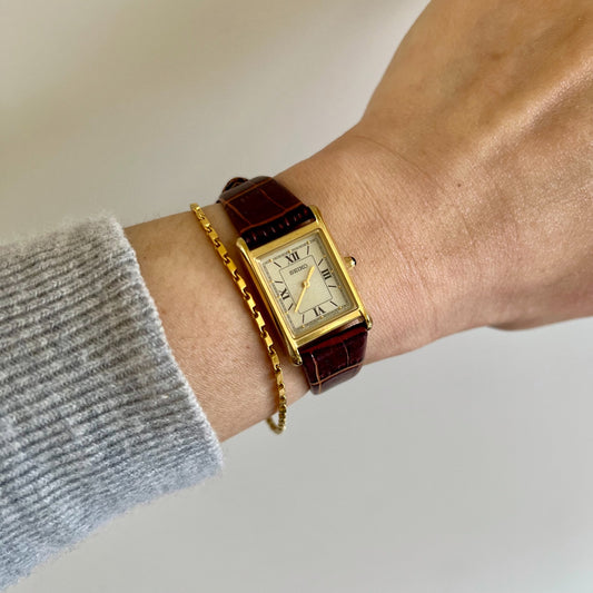 Seiko Nano Universe limited edition silver Roman dial gold tone tank watch with burgundy calf leather strap worn on the wrist beside a fine gold bracelet
