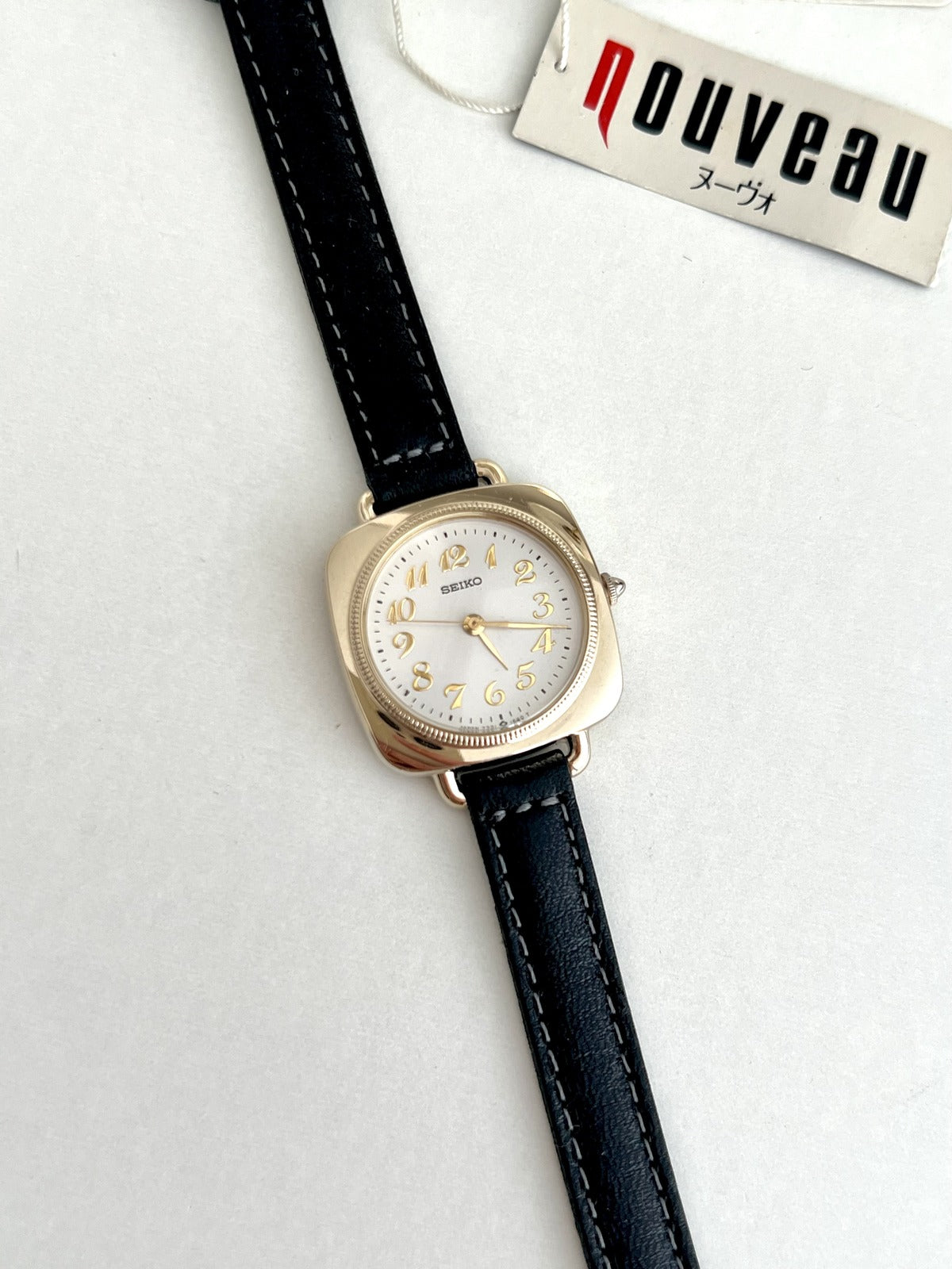 Seiko Nouveau 7321-0340 with flowing gold Arabic numerals, white dial, gold tone cushion case and stitched black leather strap.