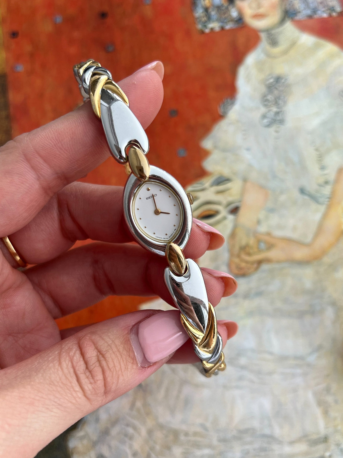 Full handheld view of the Seiko oval watch and polished sculpted silver and gold tone bracelet