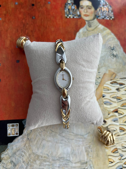 Seiko women’s watch with a white oval dial, gold dot markers and sculpted silver and gold tone bracelet on a grey cushion