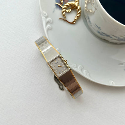 Seiko petite silver and gold bracelet watch on a white surface beside a cup and saucer.