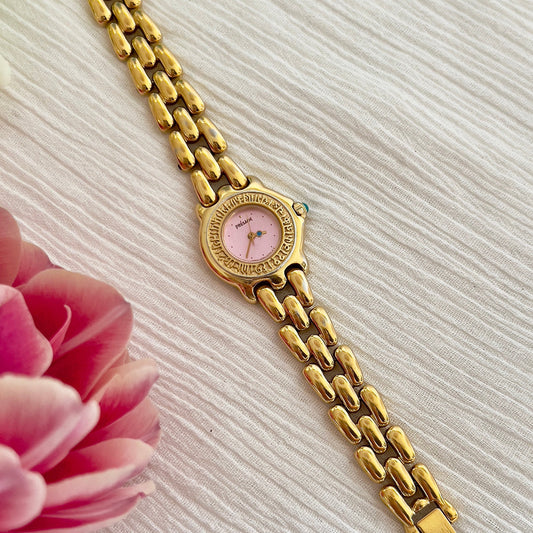 Seiko Presage gold bracelet watch with pink pearl dial and engraved bezel, displayed with a flower.