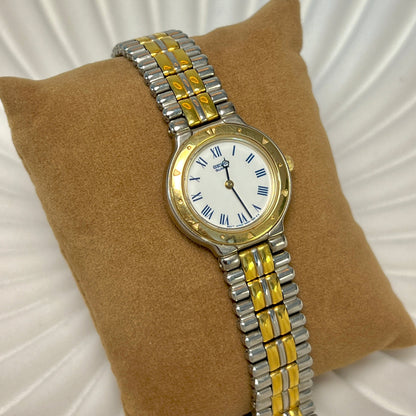 Seiko women’s two tone watch with white Roman numeral dial, gold tone decorative bezel and polished bracelet.