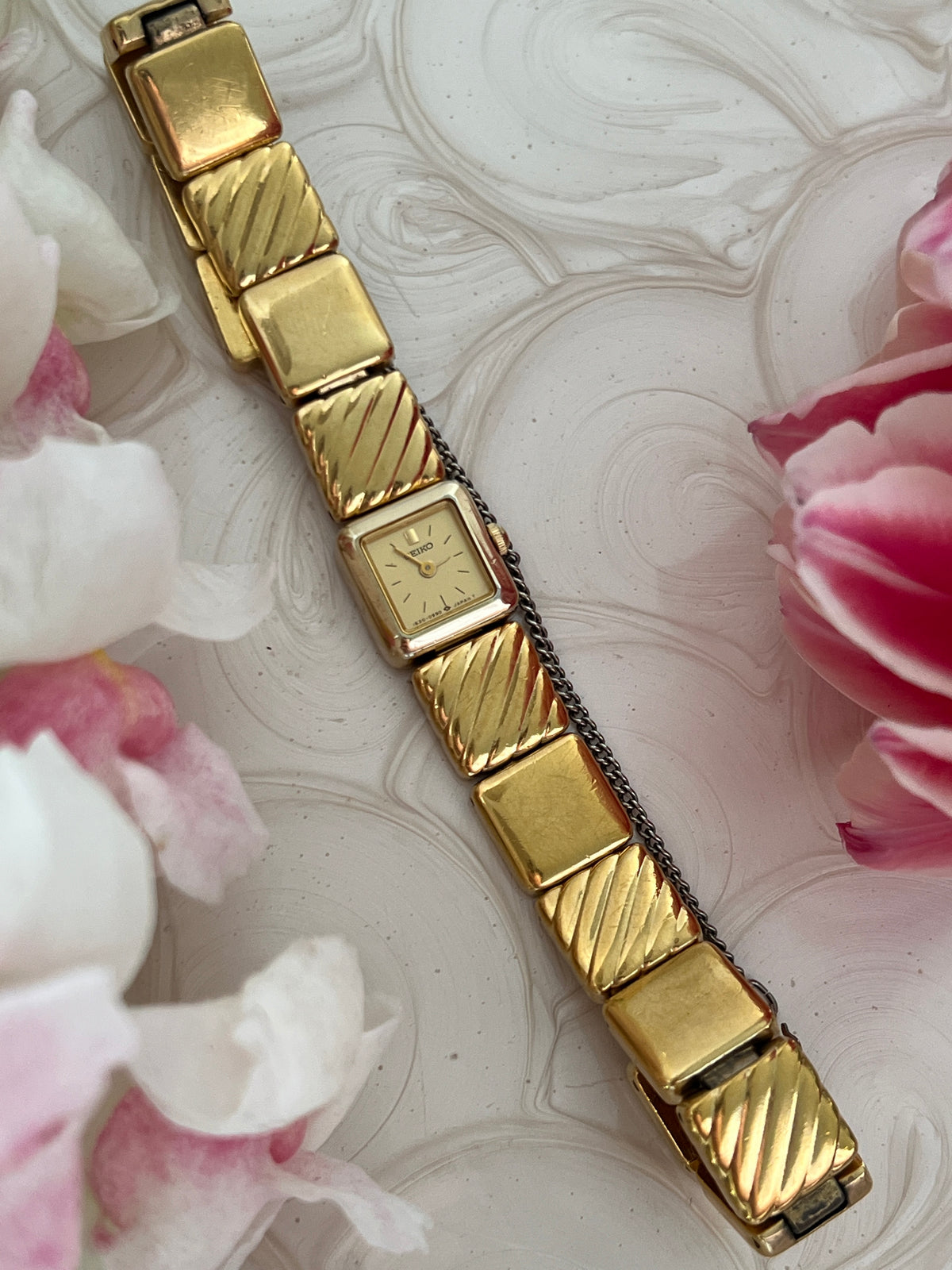 Angled view of the Seiko square gold-tone watch with sculpted bracelet.