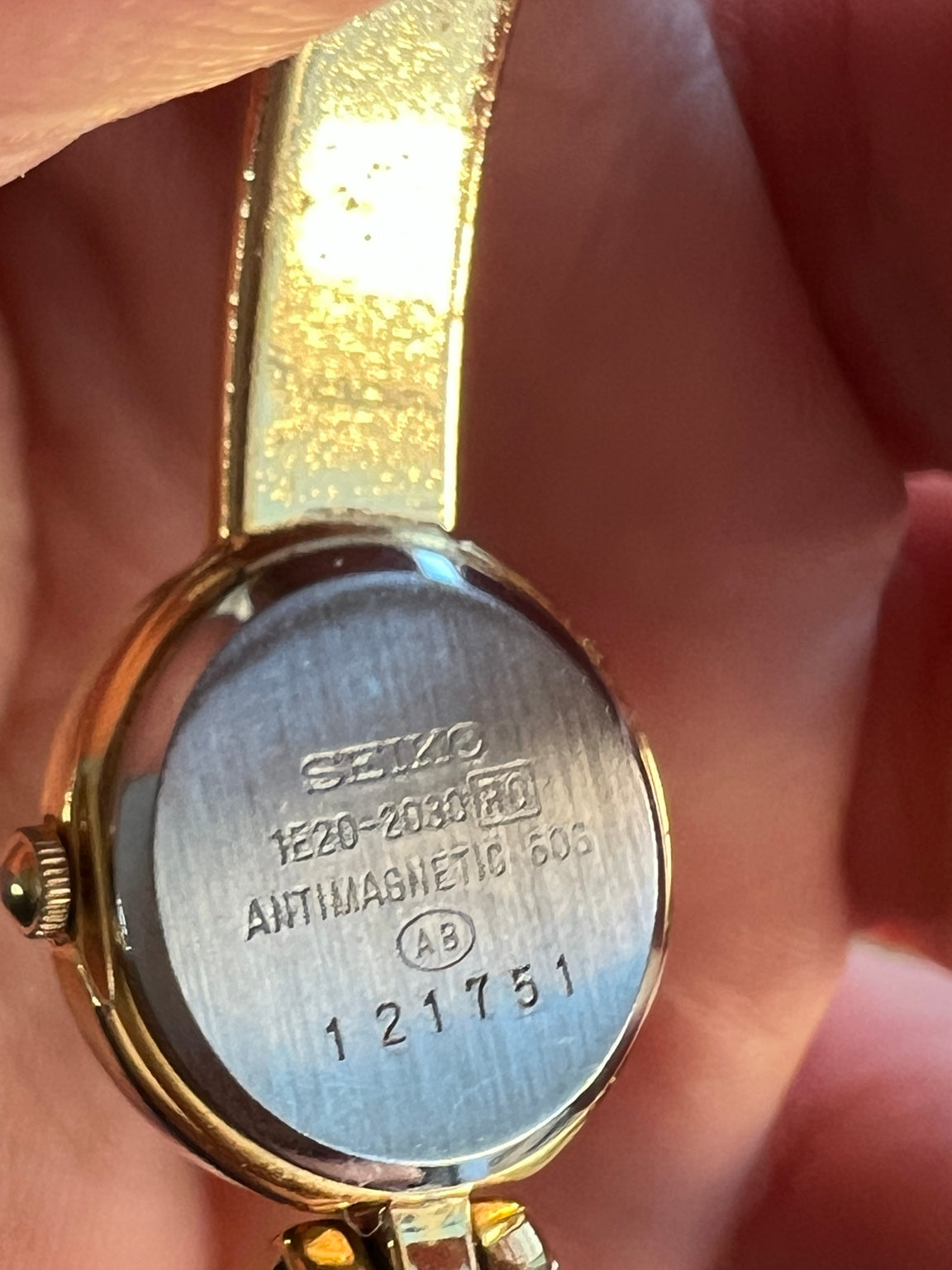 Caseback of Seiko Tissé 1E20 2030 women’s watch showing reference, serial 121751 and gold tone bangle bracelet