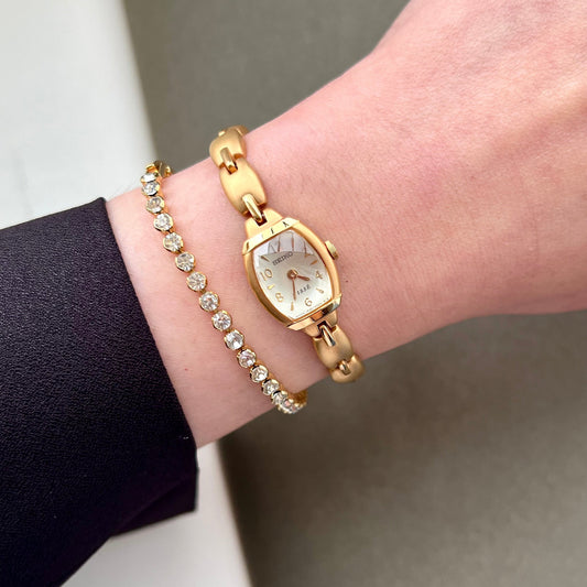 Seiko Tissé gold tone women’s watch with faceted white dial and jewellery style bracelet, worn beside a crystal bracelet