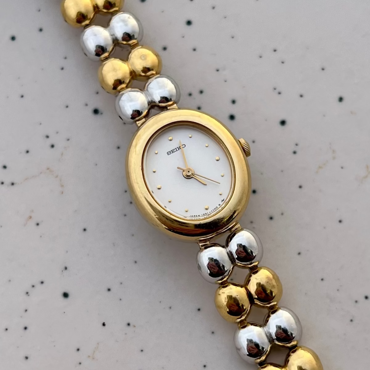 Detail of the alternating gold and silver bead bracelet on the Seiko two-tone oval women's watch.