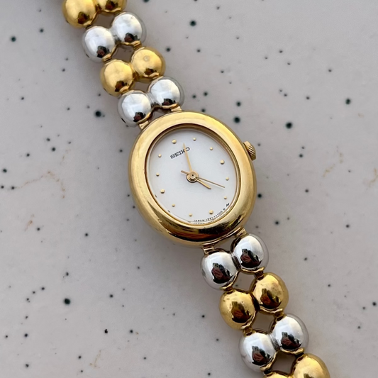 Detail of the alternating gold and silver bead bracelet on the Seiko two-tone oval women's watch.