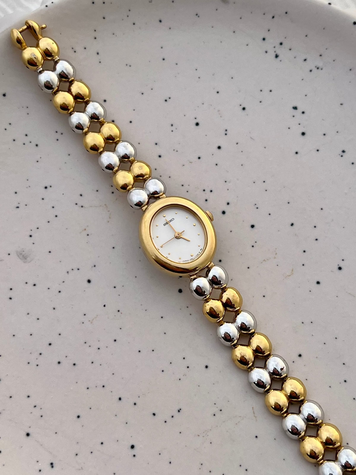 Front view of the Seiko two-tone oval watch with a white dial and gold and silver bead bracelet.