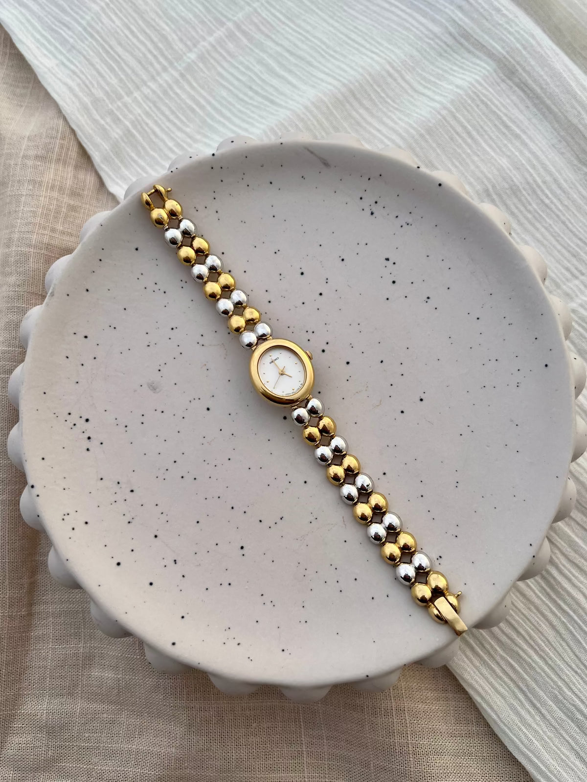 Close-up of the white dial, gilt hands and dot hour markers on the Seiko oval watch.