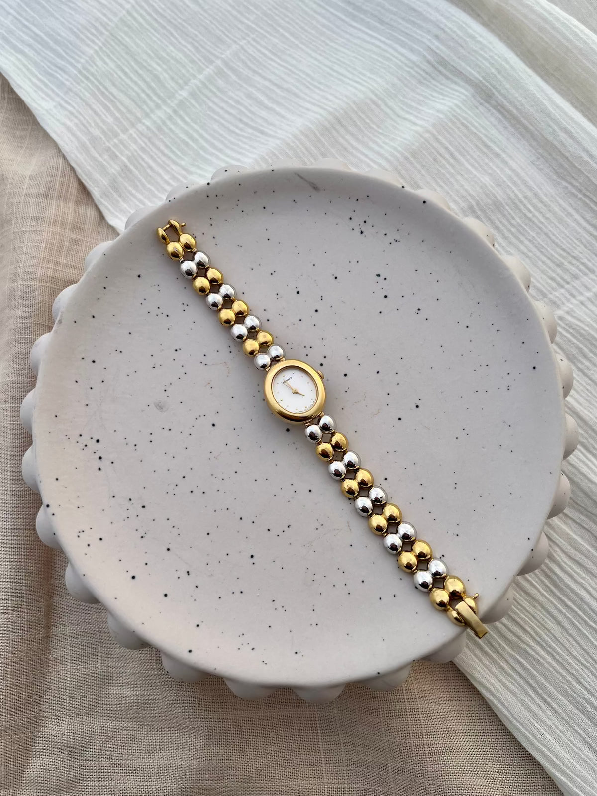 Wrist view of the Seiko two-tone oval watch with its gold and silver bead bracelet.