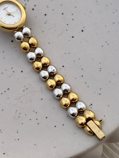 Front view of the Seiko oval women's watch with gold hands and a double-bead bracelet.
