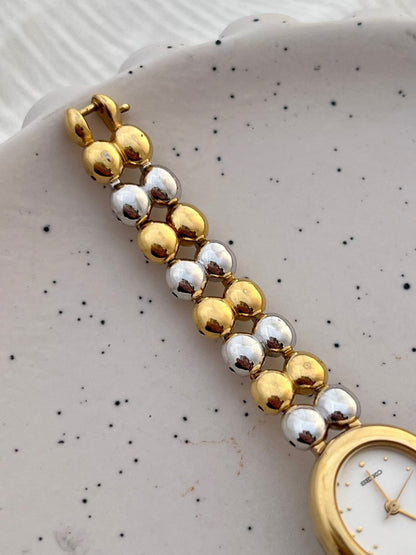 Close-up of the Seiko watch's white dial and delicate gold-tone hour markers.