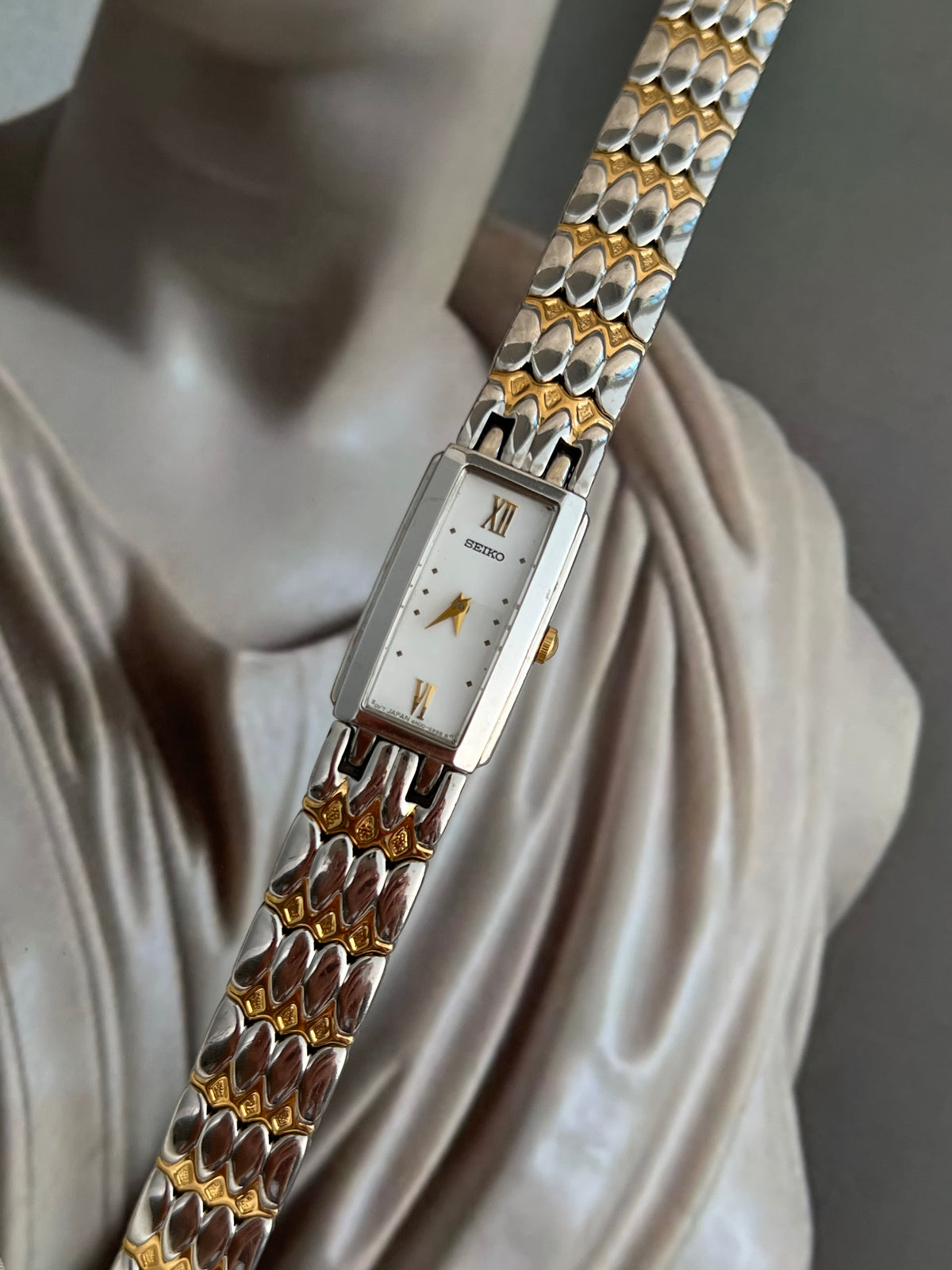 Seiko two-tone rectangular watch with white dial, gold markers and sculpted bracelet.