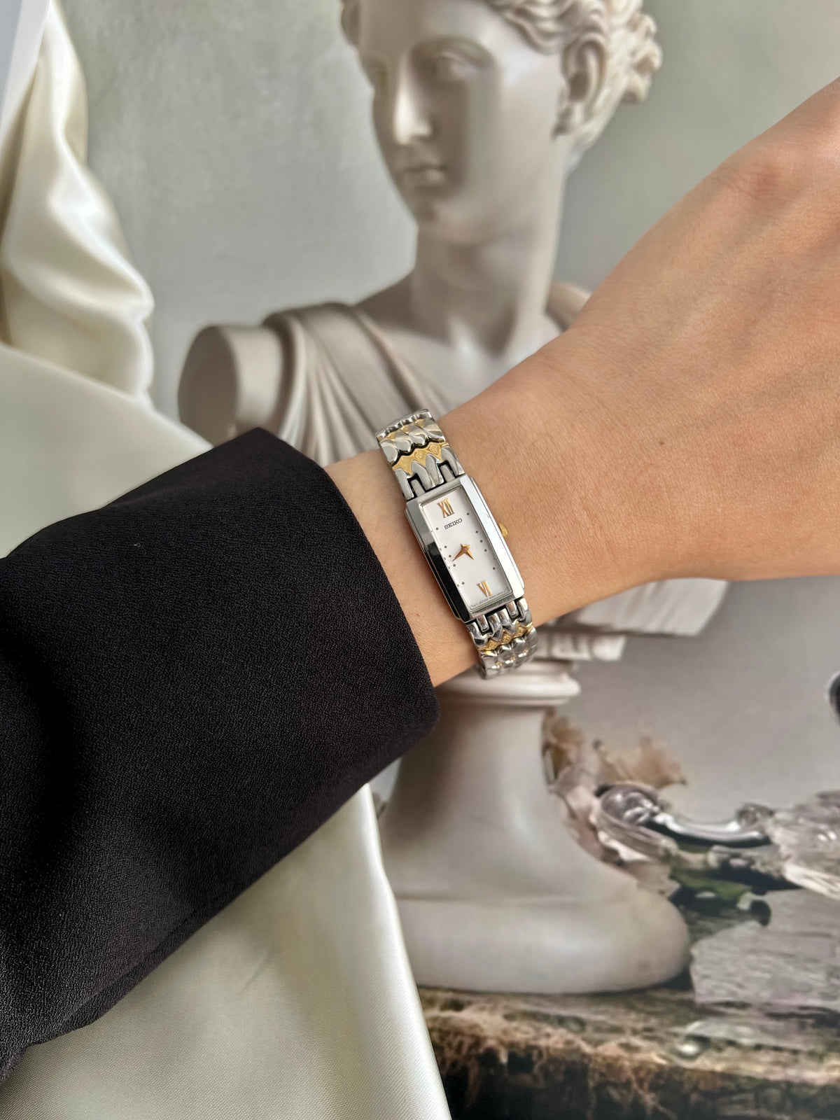 Gold-tone and silver-tone bracelet on a Seiko watch with white dial.