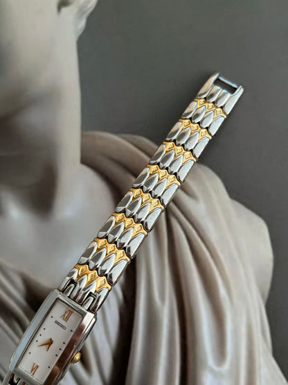 White dial Seiko watch with gold baton hands and rectangular case.