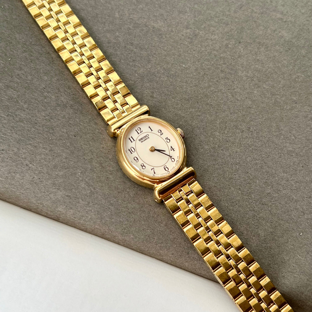 Seiko ladies gold bracelet watch with ivory dial and black numerals on wrist beside diamond tennis bracelet