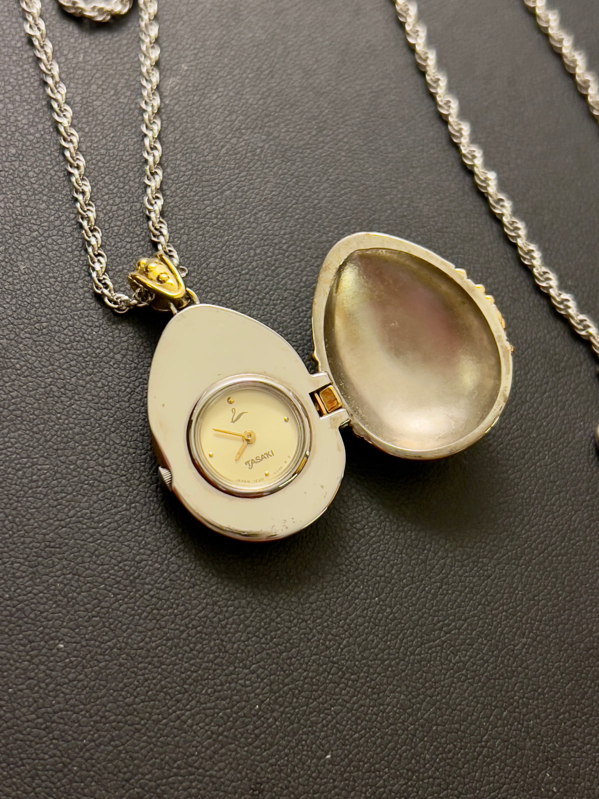 Tasaki egg pendant watch with a gold-tone case, white dial, and pearl detail.